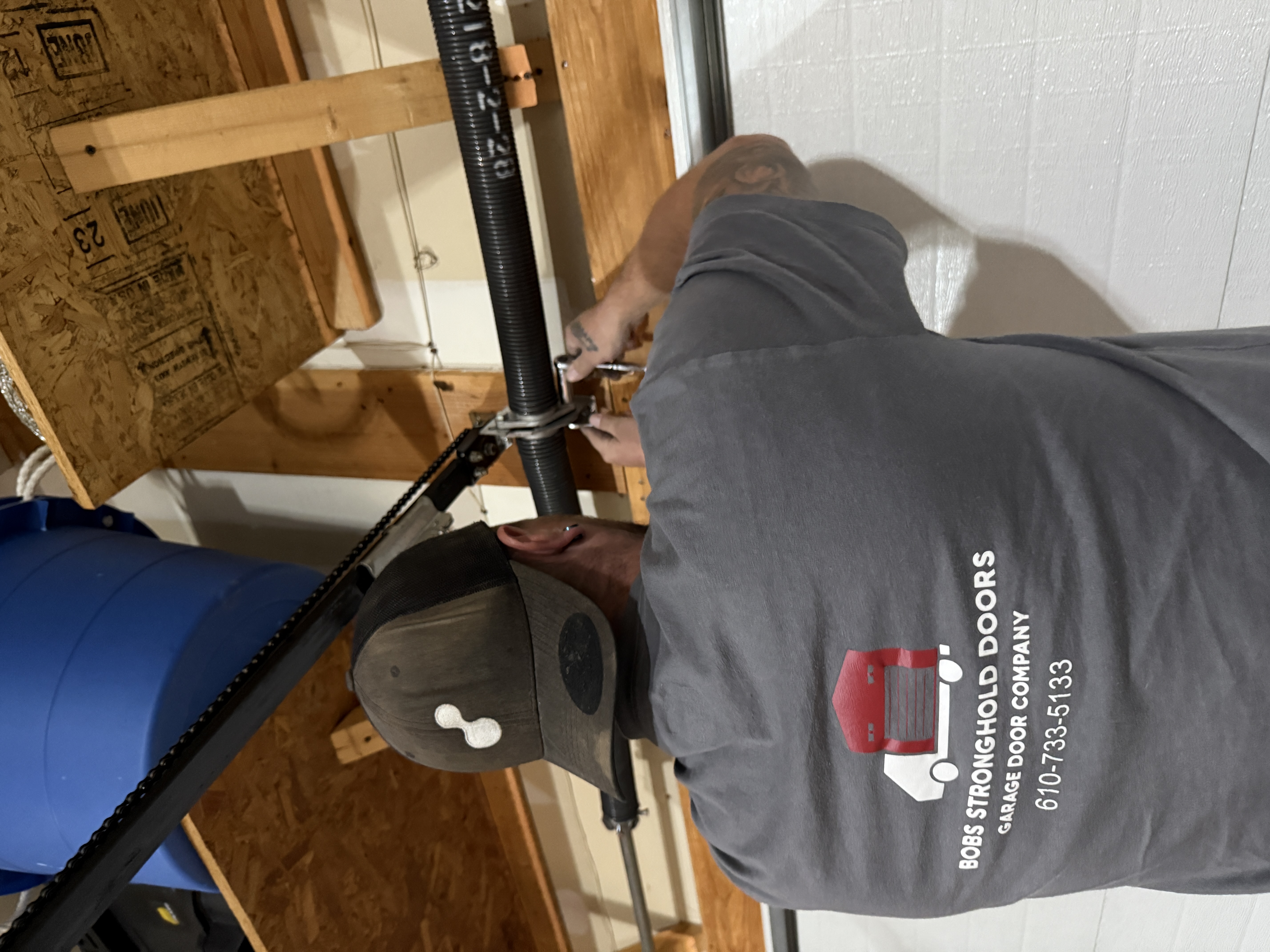 Bob's Stronghold Doors technician repairing torsion spring in branded shirt