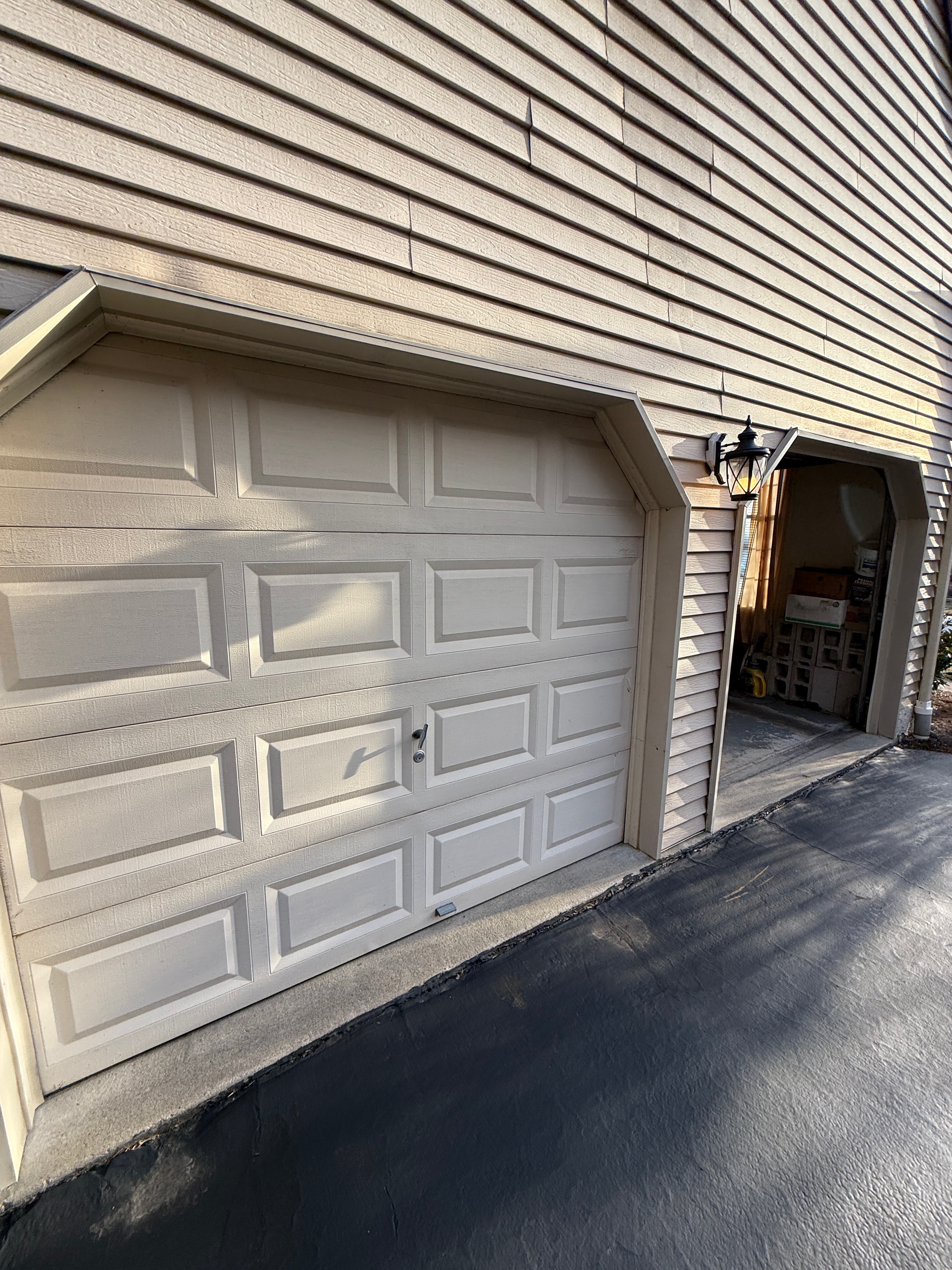 Beige garage door with vinyl siding serviced by Bob's Stronghold Doors